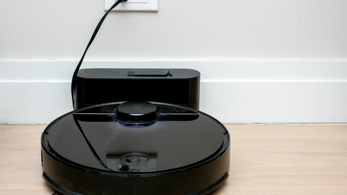 A Roborock robot vacuum cleaner docked at its charging station, photographed at floor level.