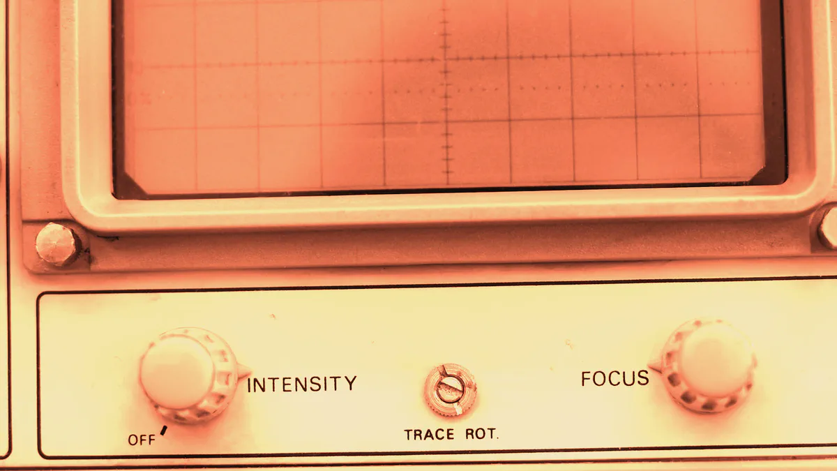 Terracotta-toned photograph of an analogue oscilloscope face showing an empty measurement graticule above INTENSITY and FOCUS controls.
